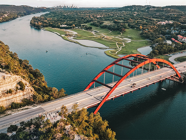 Luftaufnahme eines Flusses und einer Brücke in Austin, Texas, mit der Stadt im Hintergrund. 