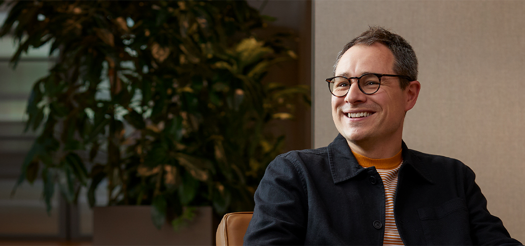 肘掛け椅子に座ってほほ笑み、自身の右側にいる人を見つめるダン。