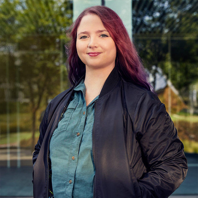 Alexa steht draußen und blickt in die Kamera.