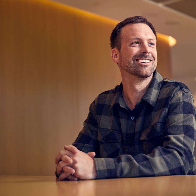 Jordan sitzt lächelnd am Tisch und hat die Hände vor sich gefaltet.