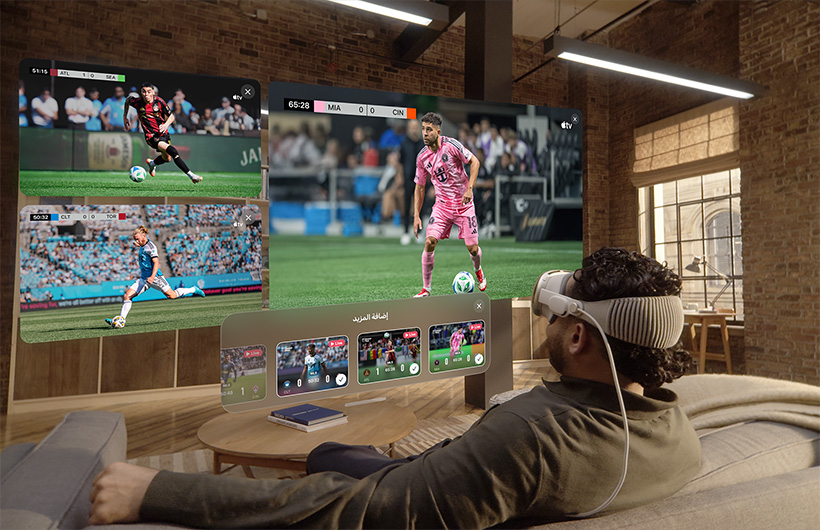 شخص يضع Apple&nbsp;Vision&nbsp;Pro على وجهه ويجلس على أريكة في غرفة الجلوس، وأمامه شاشة كبيرة إلى جانب شاشتين أصغر حجماً، وكل واحدة منها تعرض فعالية رياضية مختلفة. وفي أسفل الشاشة الكبيرة، تظهر نافذة اختيار كُتبت عليها عبارة إضافة المزيد